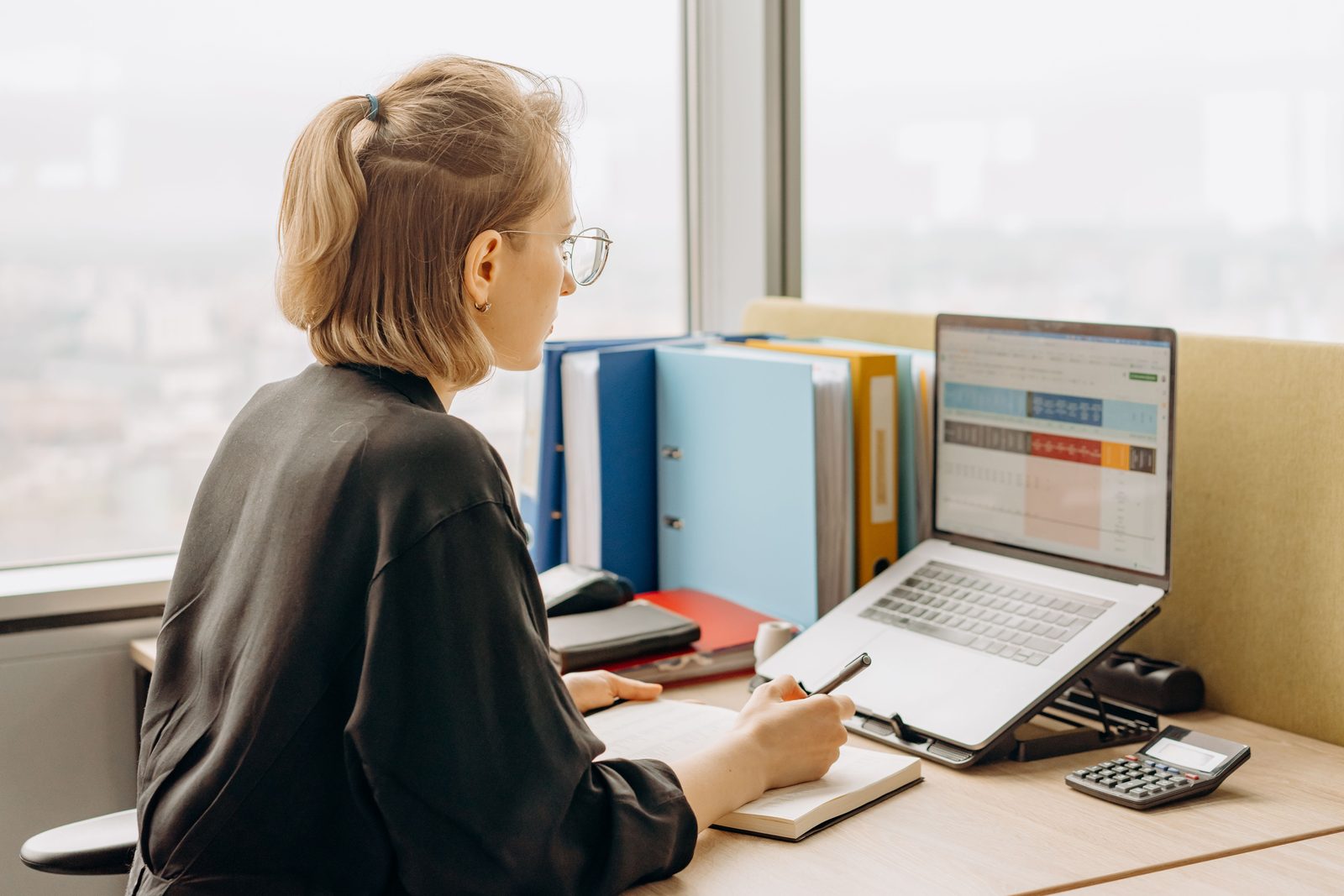 Professional learner working with a spreadsheet on a laptop and taking notes